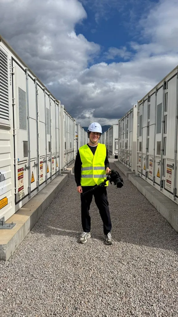 Antoine Similon in a hard hat and safety vest, camera gimbal in hand between rows of battery units