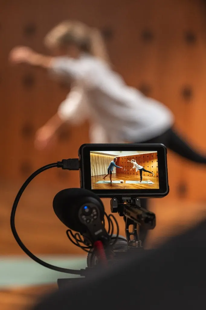 Camera monitor showing two people in a wood-panelled studio