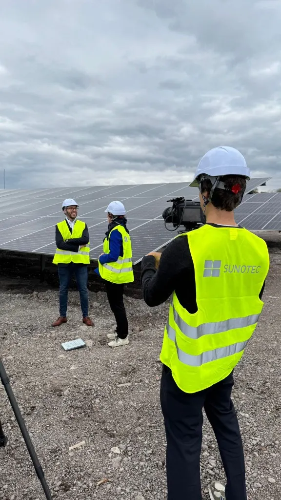 Crew filming two people in high-visibility vests among solar panels